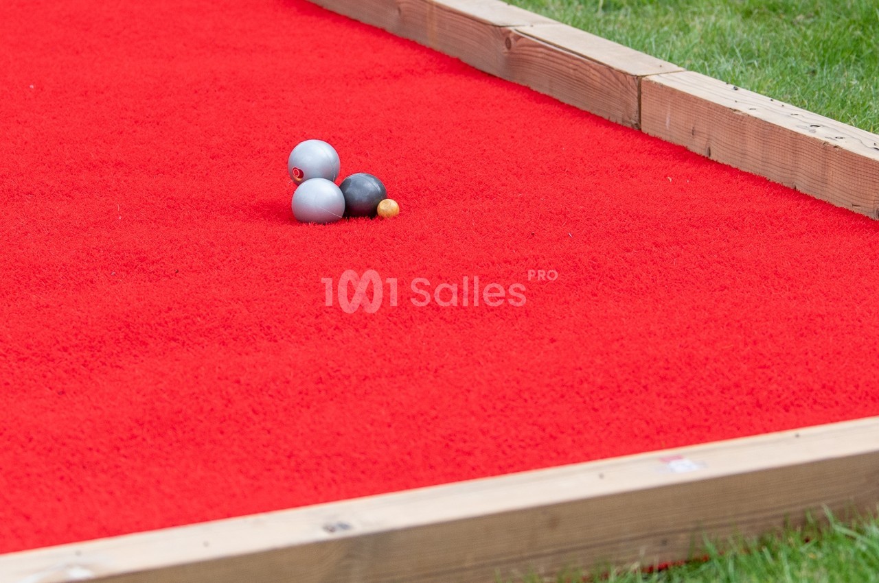 Terrain de pétanque avec tapis rouge, trois boules métalliques et un cochonnet posés au centre.