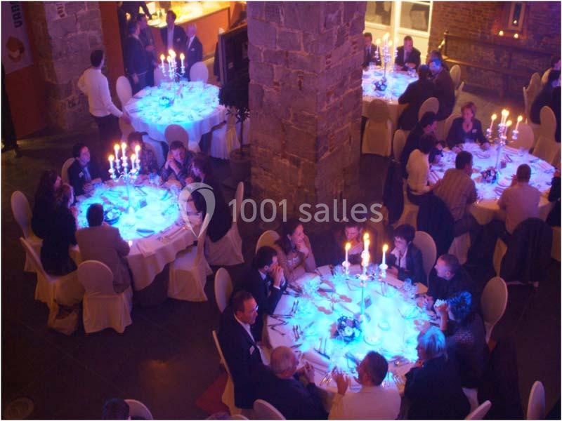 Des convives dînent autour de tables rondes éclairées de bougies dans une salle à l'ambiance tamisée.