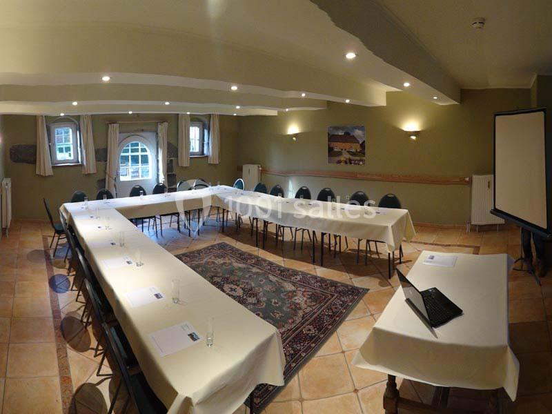 Salle de réunion lumineuse avec tables disposées en U, chaises alignées, projecteur et documents sur les tables.