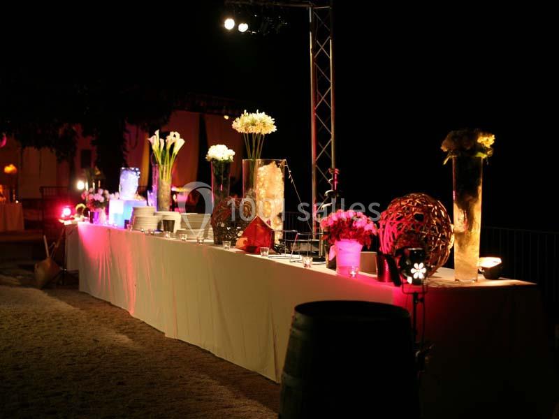 Table de buffet éclairée la nuit, décorée de vases avec fleurs et éléments lumineux.