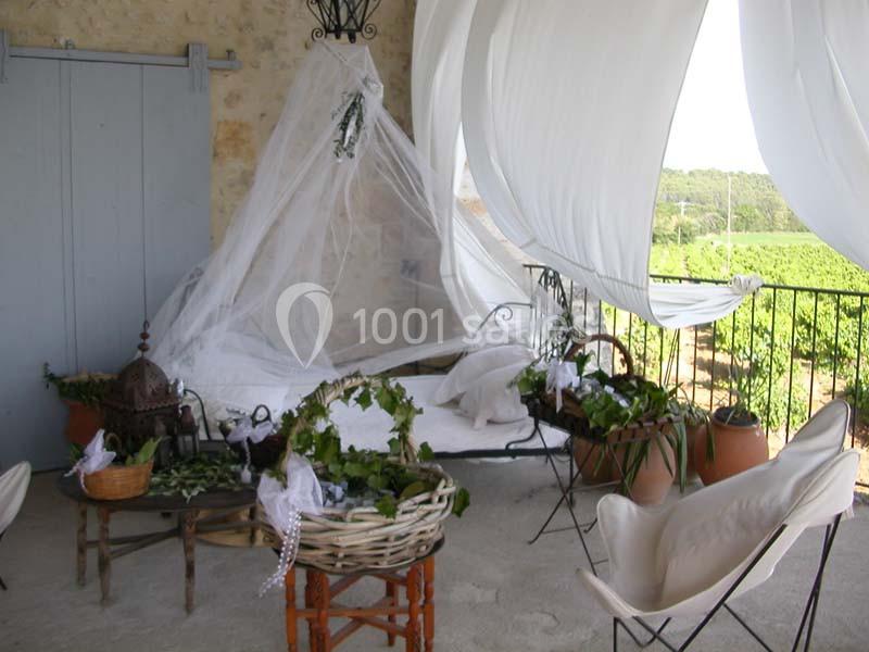 Terrasse décorée avec un lit à baldaquin en voile blanc, des plantes en paniers et vue sur des vignes en arrière-plan.