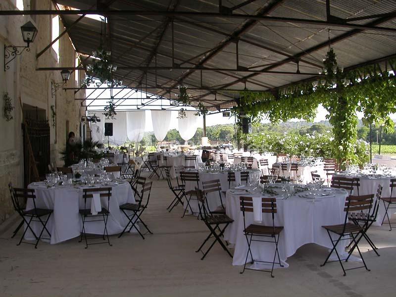 Salle de réception en plein air avec tables rondes dressées, nappes blanches et décoration végétale suspendue.