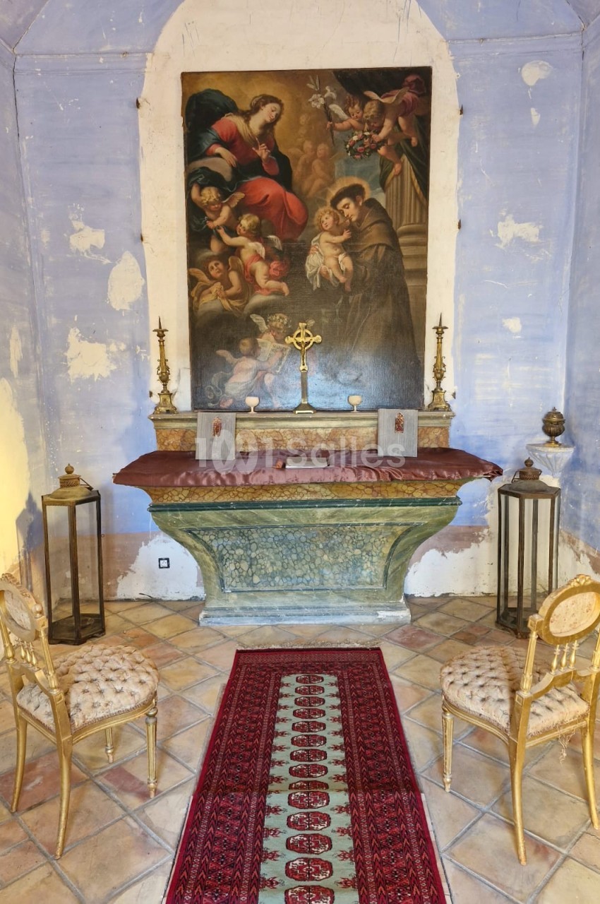 Autel ancien avec tableau religieux, croix dorée, chandeliers et deux chaises dans une petite chapelle aux murs patinés.