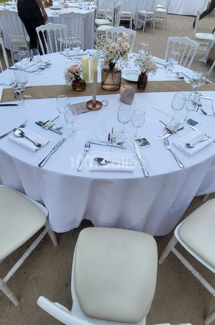 Table ronde dressée pour un événement, avec nappes blanches, couverts, verres et centre de table floral.