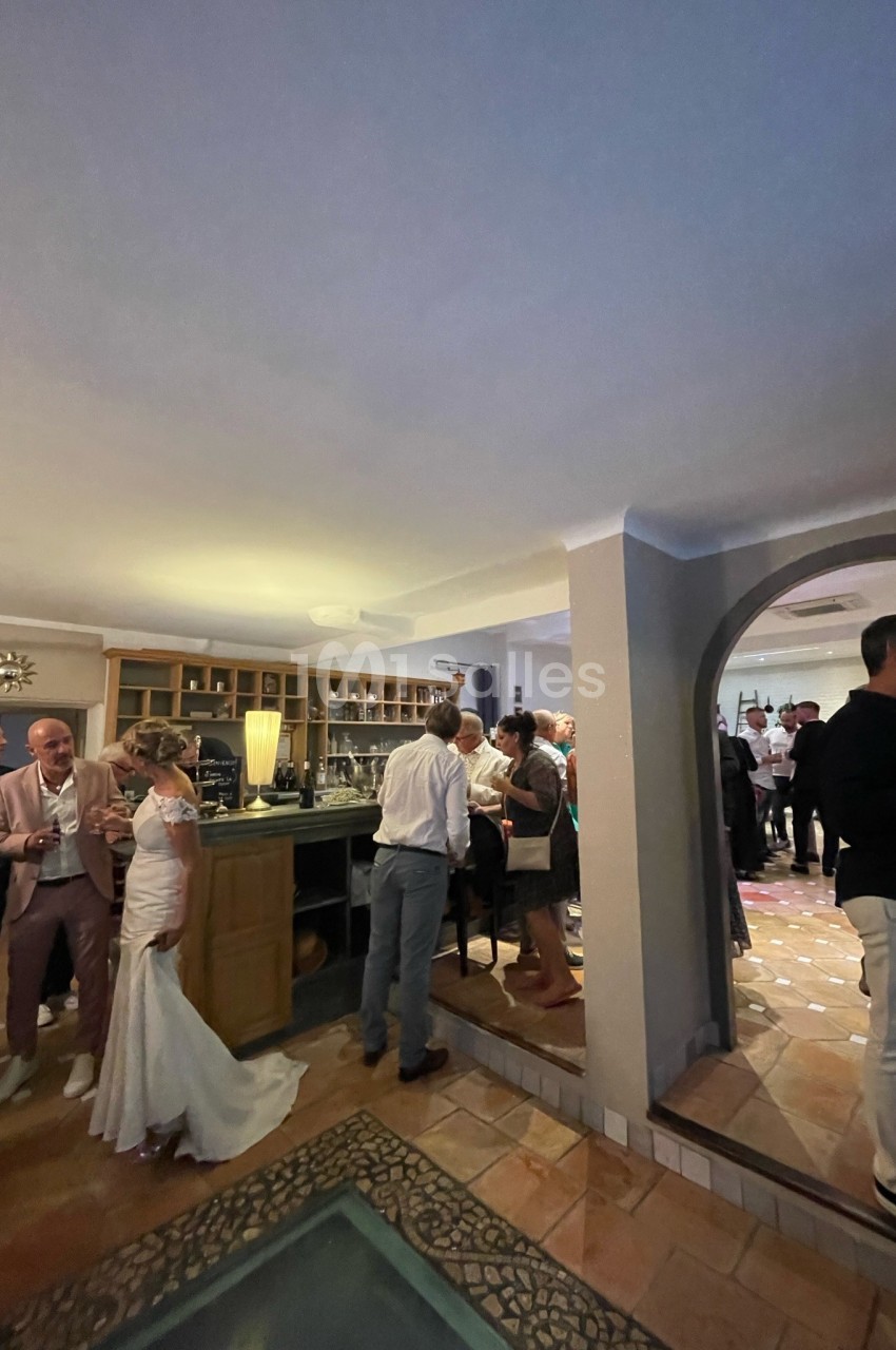 Des invités discutent dans une salle de réception avec un bar, lors d'un événement festif en intérieur.