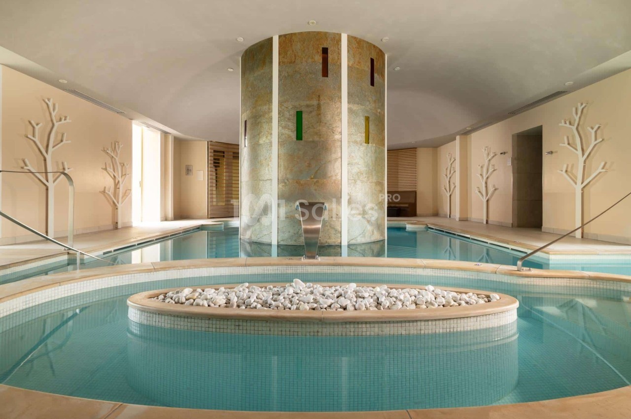 Piscine intérieure avec jets d'eau, décorée de pierres blanches et entourée de murs ornés de motifs d'arbres.