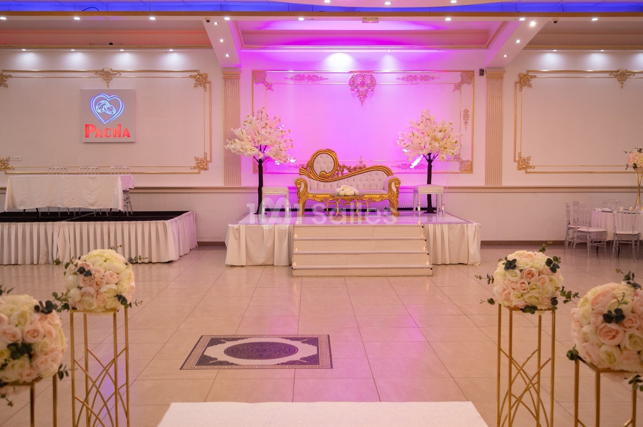 Salle de réception décorée avec un canapé doré sur une estrade, éclairage rose et arrangements floraux.