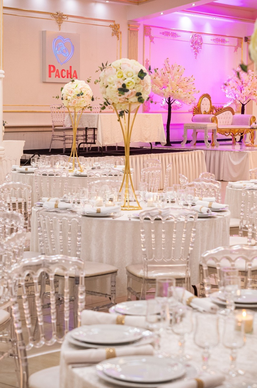 Salle de réception élégante avec tables rondes décorées de nappes blanches, chandeliers et fleurs, éclairage rose en arrière…