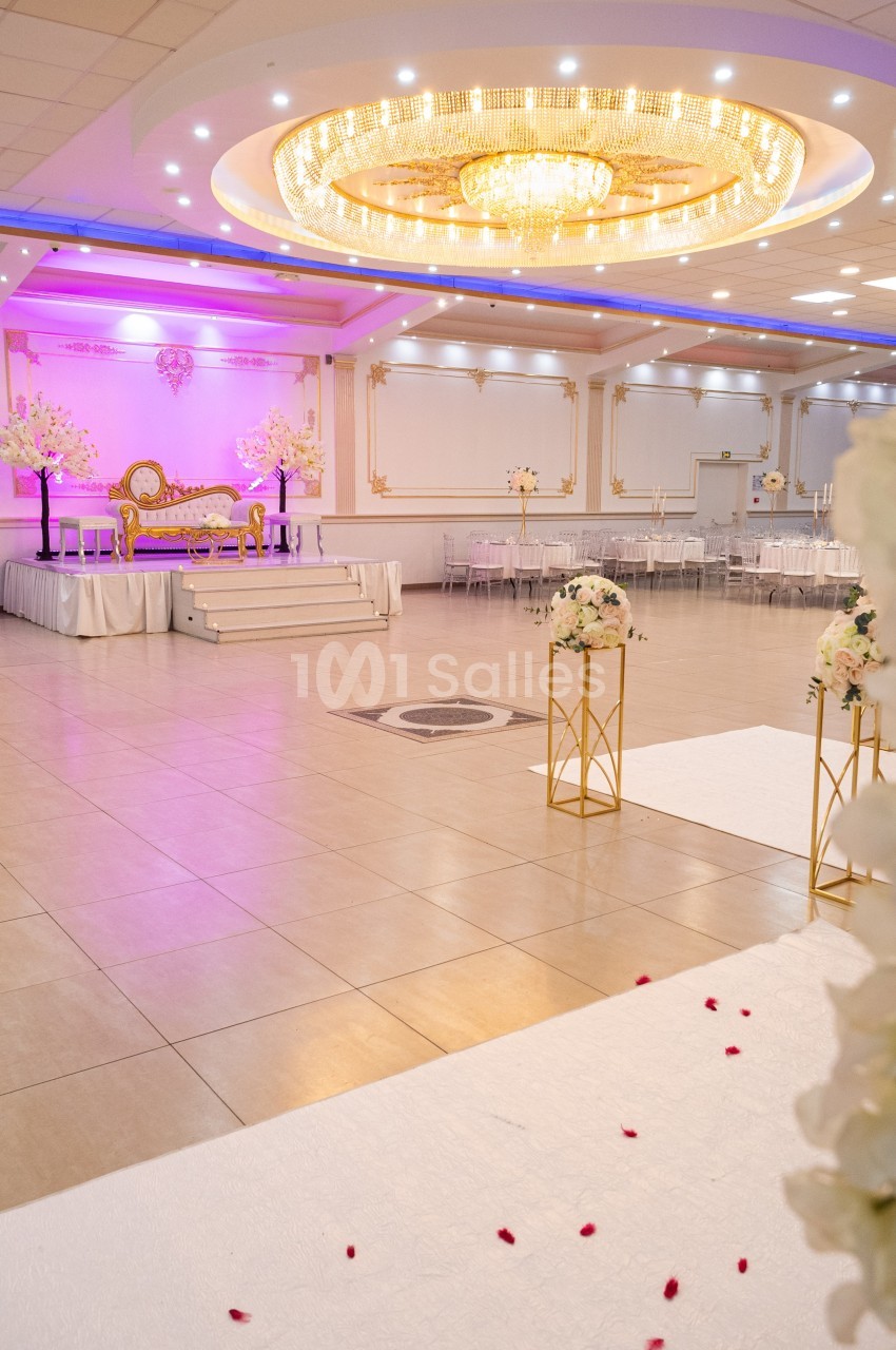 Salle de réception décorée avec un lustre central, une scène ornée d'un canapé doré et des arrangements floraux.