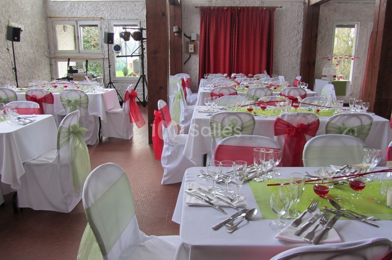 Salle de réception décorée avec des nappes blanches, des rubans colorés sur les chaises et des tables dressées.