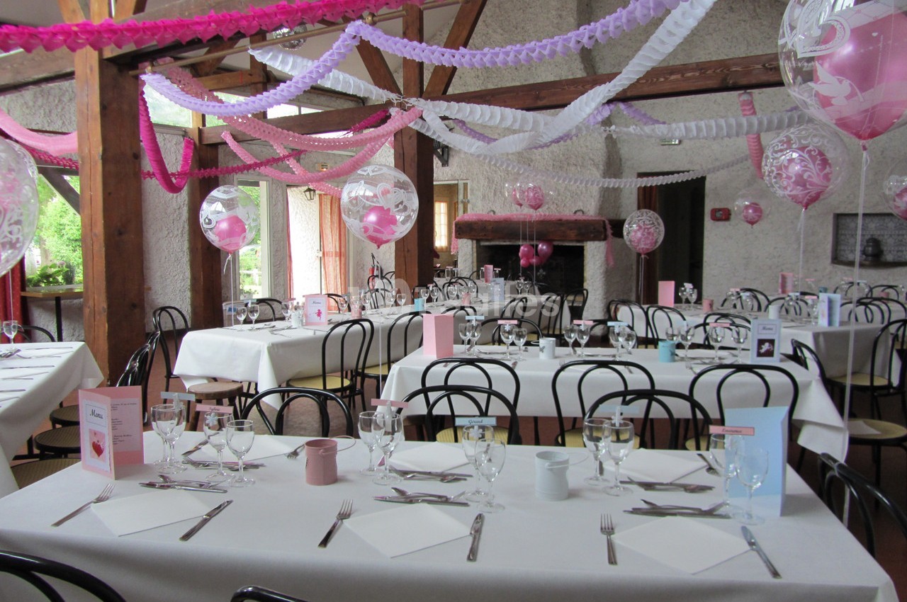 Salle décorée pour une réception avec tables dressées, guirlandes colorées et ballons suspendus.