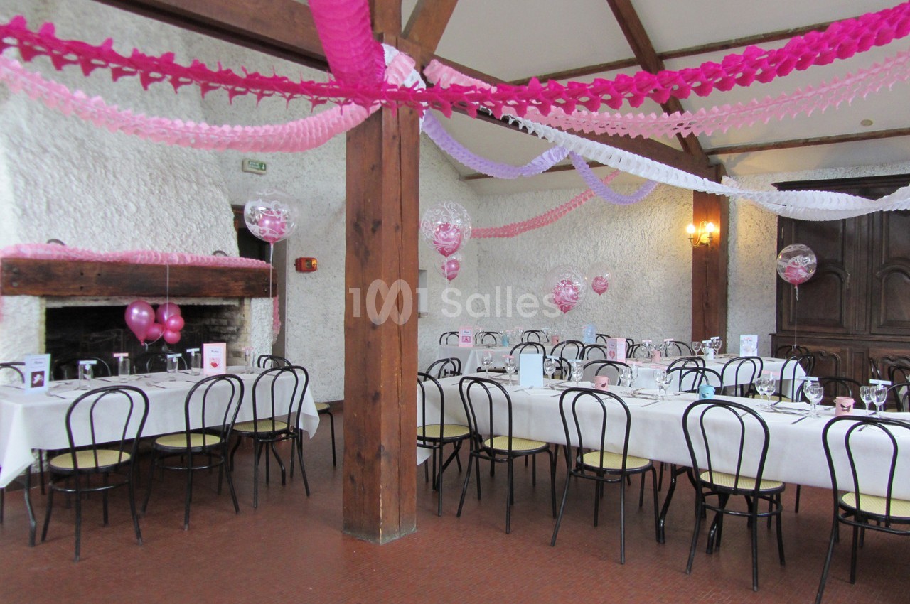 Salle décorée avec des guirlandes roses et blanches, tables dressées pour un événement festif.