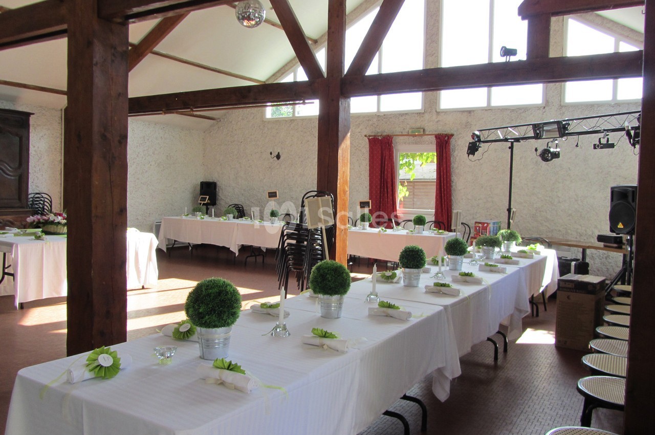 Salle de réception lumineuse avec de longues tables décorées de nappes blanches et de centres de table végétaux.