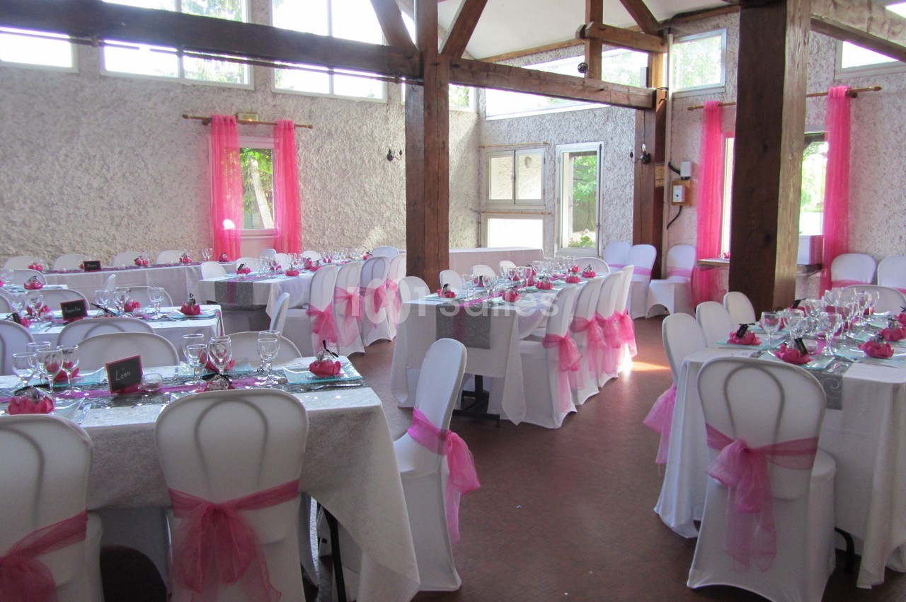 Salle de réception décorée avec des nappes blanches, des chaises ornées de nœuds roses et des tables dressées.