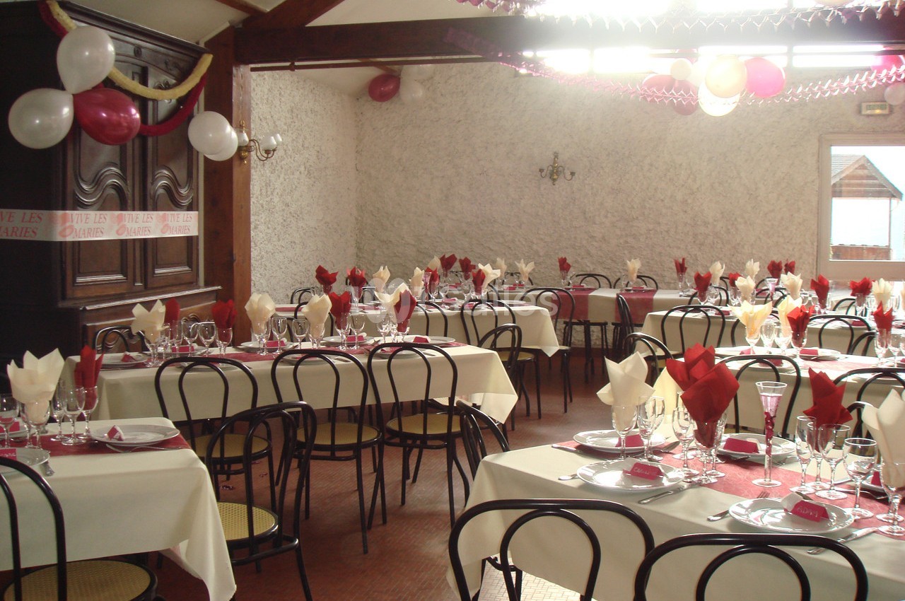 Salle décorée pour un événement avec tables dressées, nappes blanches, serviettes rouges et ballons suspendus.