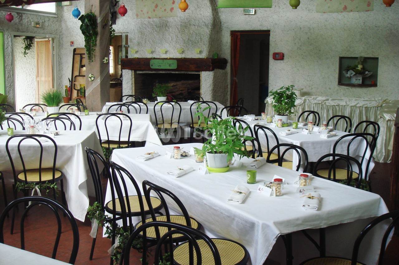 Salle de réception décorée avec des plantes, des nappes blanches et des chaises noires autour de tables dressées.