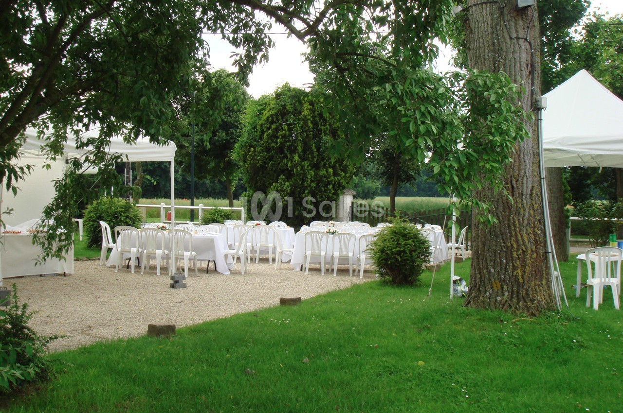 Tables et chaises blanches disposées sous des tonnelles dans un jardin verdoyant pour un événement en plein air.