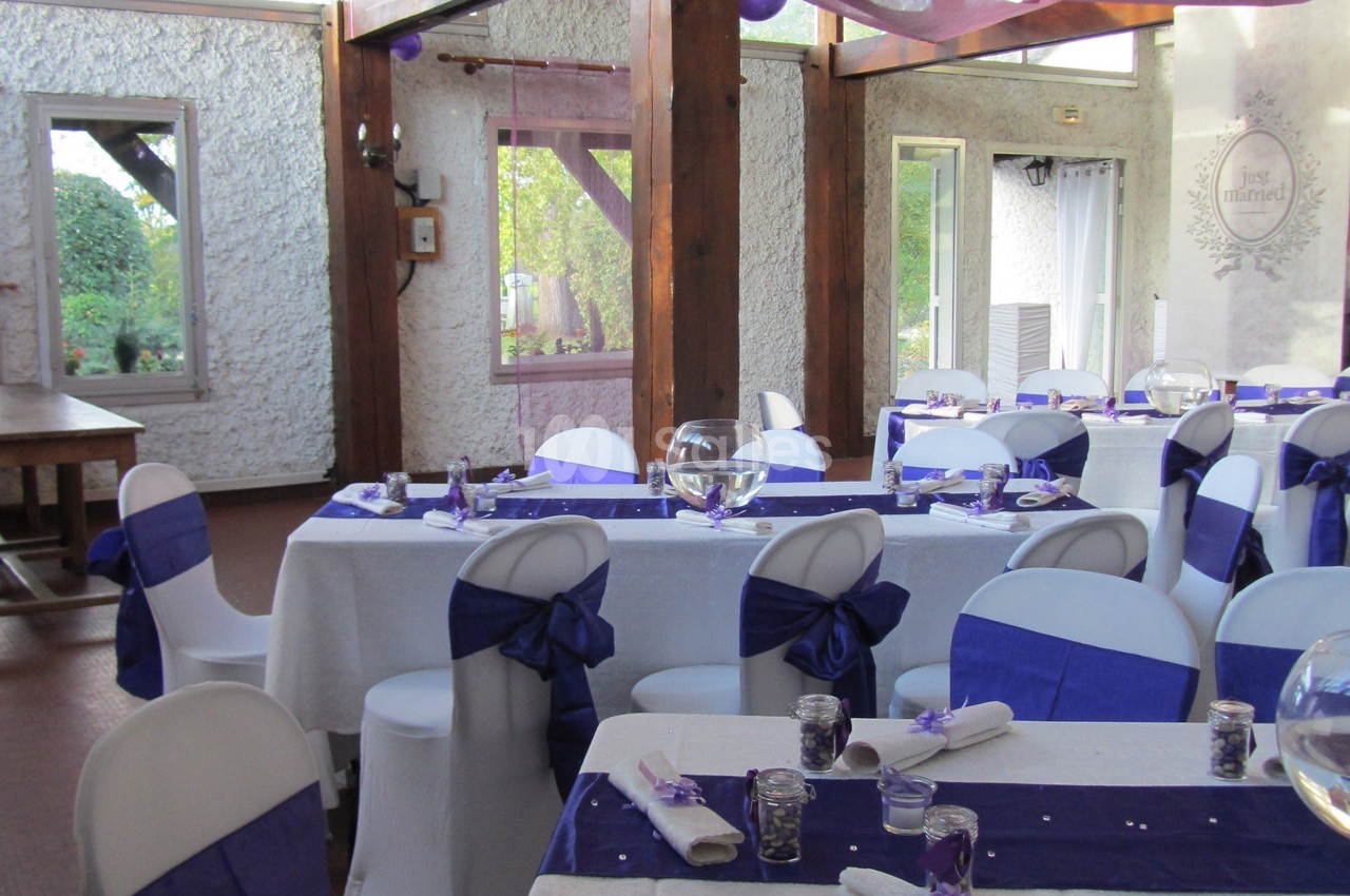 Salle de réception décorée avec des nappes blanches, des rubans violets et des centres de table en verre.