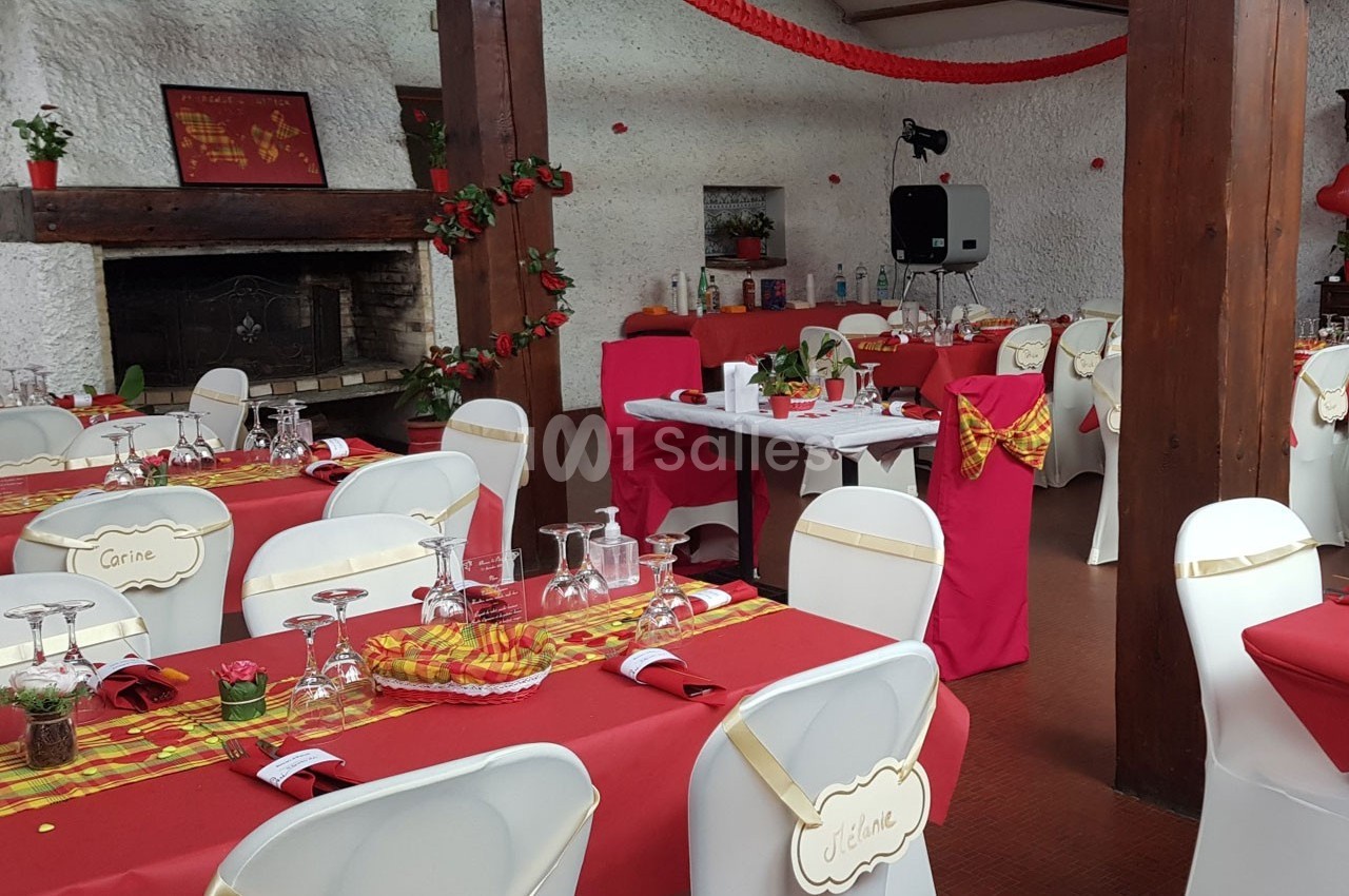 Salle décorée pour un événement, avec tables dressées en rouge et blanc, nappes colorées et éléments festifs.