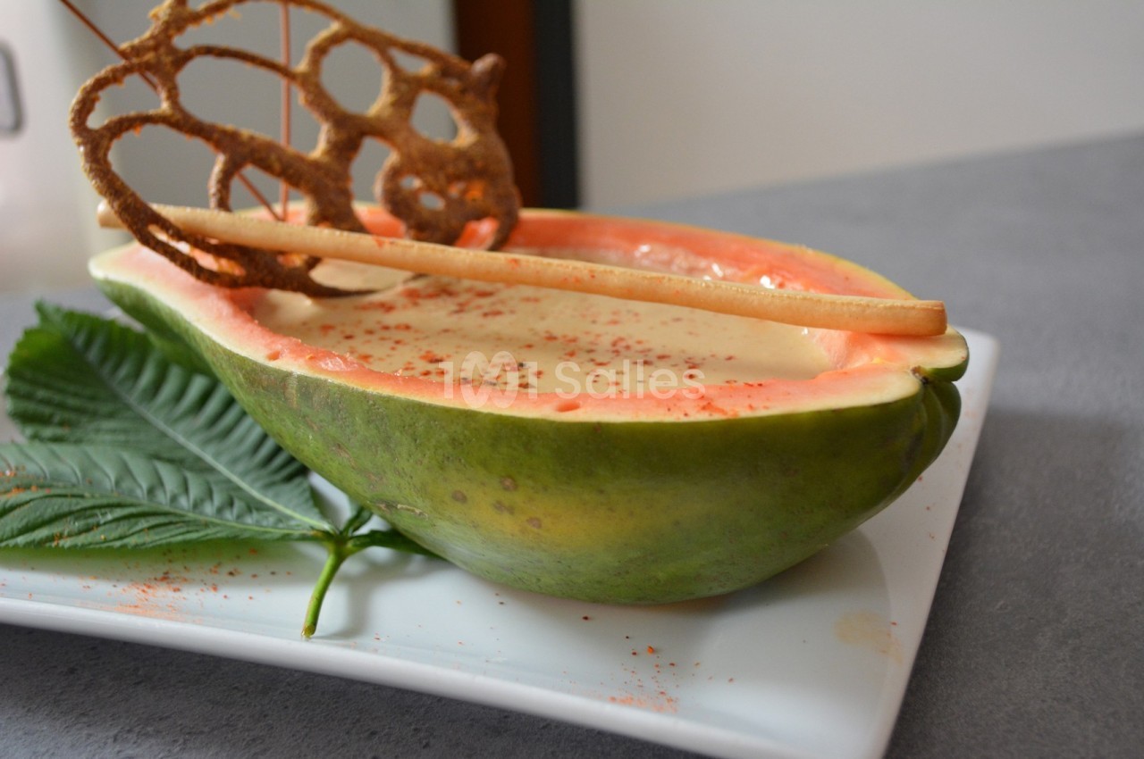 Demi-papaye remplie de mousse, décorée de croustillants et posée sur une assiette blanche avec une feuille verte.