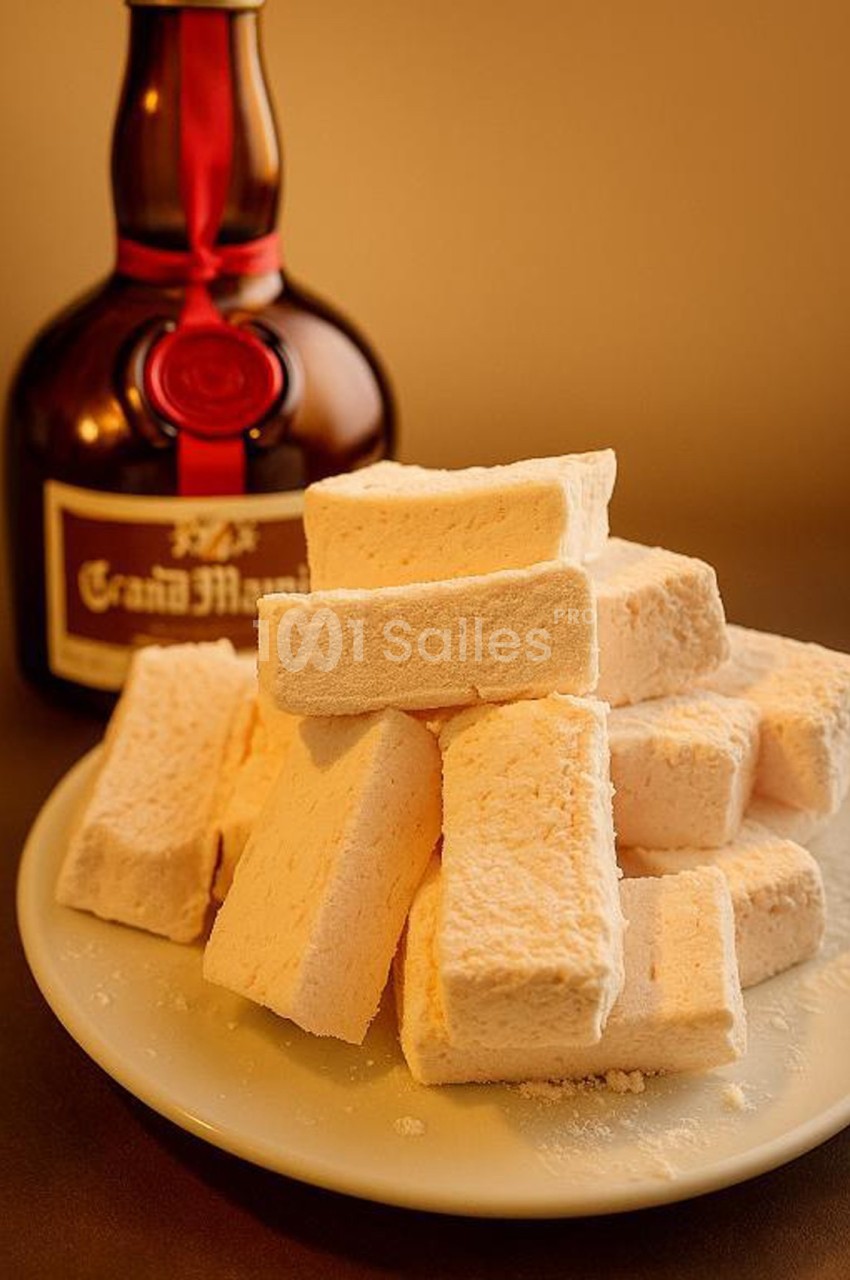 Assiette de guimauves empilées devant une bouteille de liqueur avec un ruban rouge.