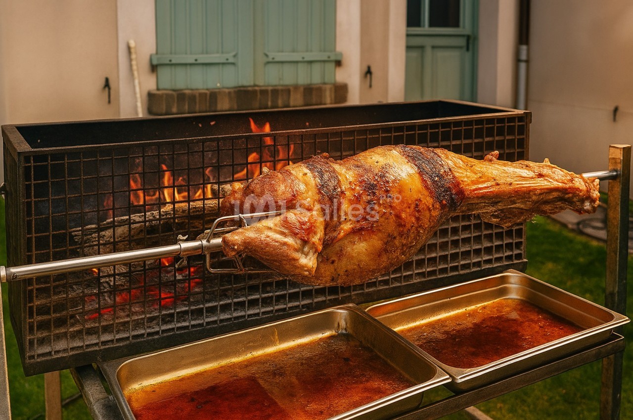 Agneau entier rôti à la broche au-dessus d'un feu de bois, avec des plats en dessous pour recueillir les jus.