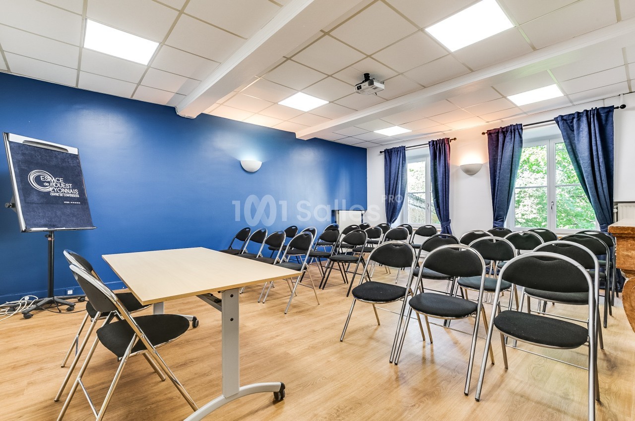 Salle de réunion lumineuse avec murs bleus, chaises noires alignées, tableau de conférence et fenêtres donnant sur des…