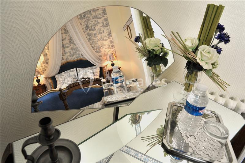Reflet d'une chambre élégante avec lit à baldaquin, fleurs et bouteilles d'eau sur une table en miroir.