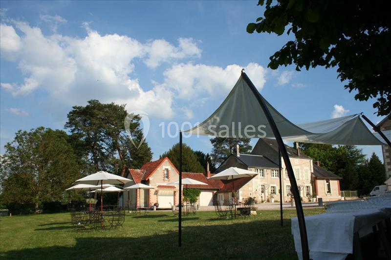 Jardin avec tables et parasols, entouré de bâtiments anciens sous un ciel bleu partiellement nuageux.