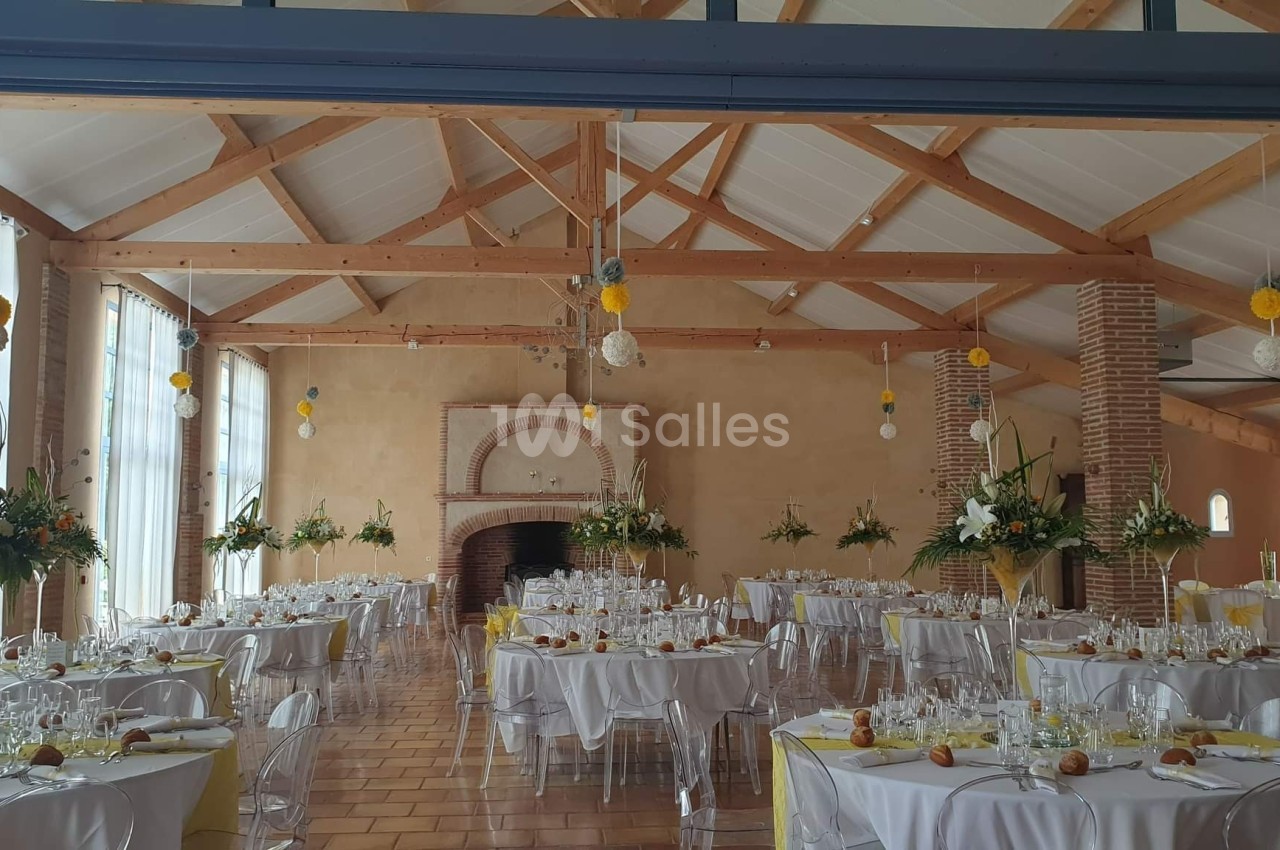 Salle de réception décorée pour un événement, avec tables dressées, chaises transparentes et compositions florales.