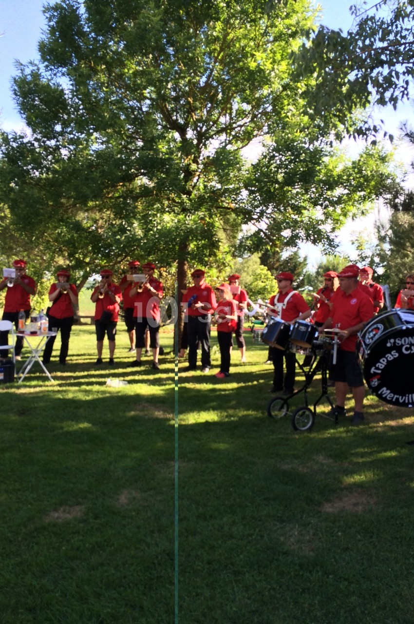 Un groupe de musiciens en tenue rouge joue dans un parc verdoyant sous un ciel ensoleillé.