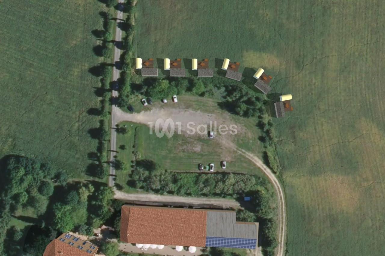 Vue aérienne d'un terrain avec des bâtiments, des véhicules stationnés et des structures alignées en bordure d'un champ.