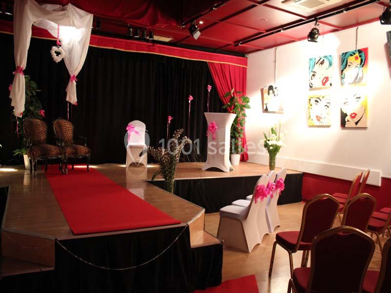 Salle décorée avec un tapis rouge, des chaises ornées de rubans roses et des œuvres d'art accrochées au mur.