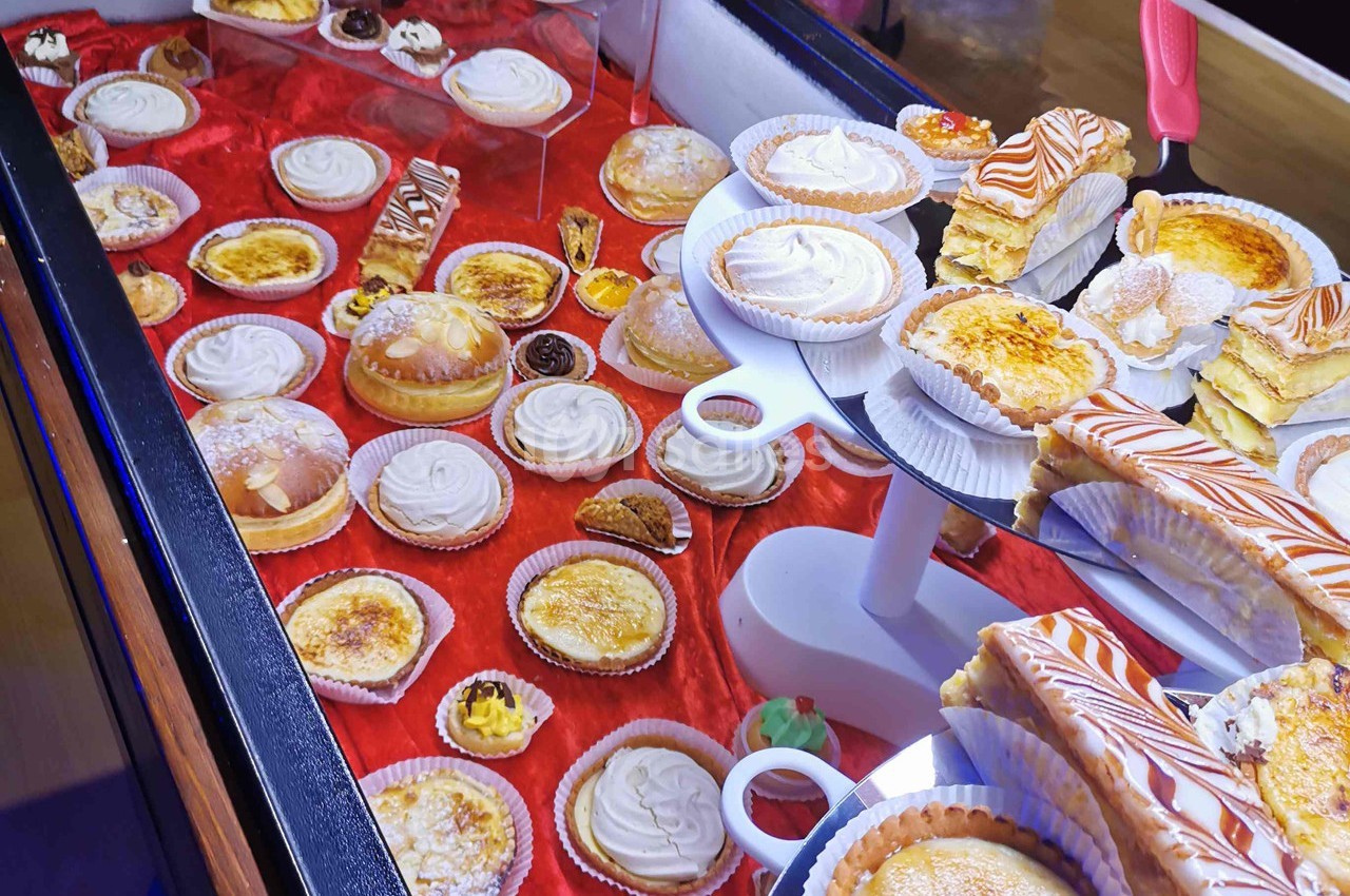 Vitrine présentant une variété de pâtisseries sur un fond rouge, incluant tartes, éclairs et gâteaux individuels.