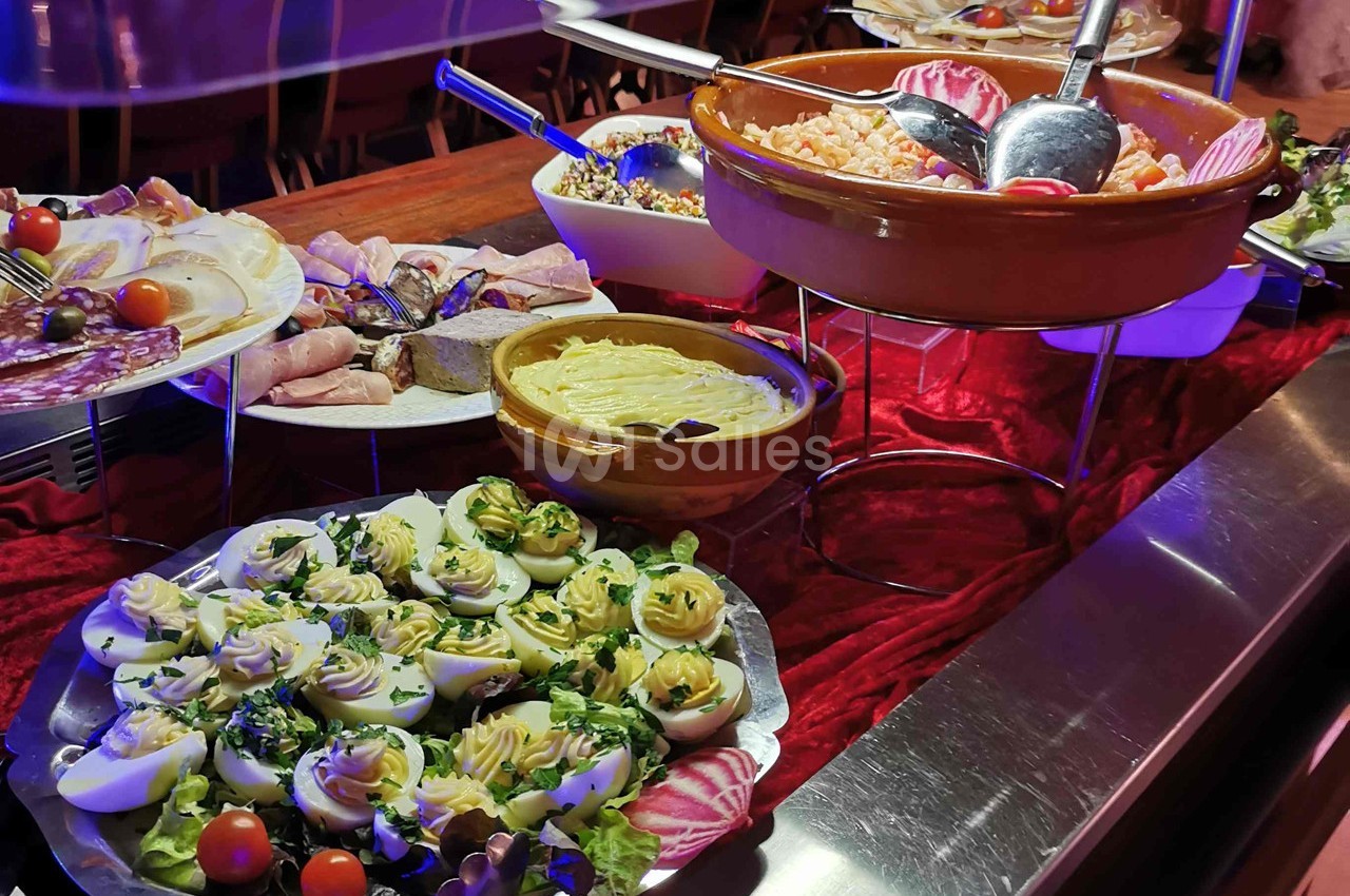 Buffet avec œufs mimosa, charcuterie, crudités et plats variés présentés sur une nappe rouge.