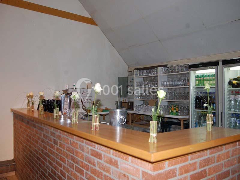 Comptoir en bois avec des vases contenant des fleurs, devant des étagères remplies de verres et de bouteilles.