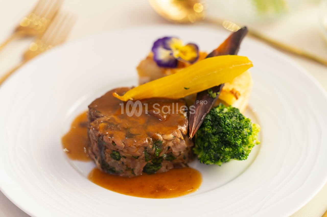 Assiette gastronomique avec un médaillon de viande en sauce, légumes colorés et purée, présentée sur une table élégante.