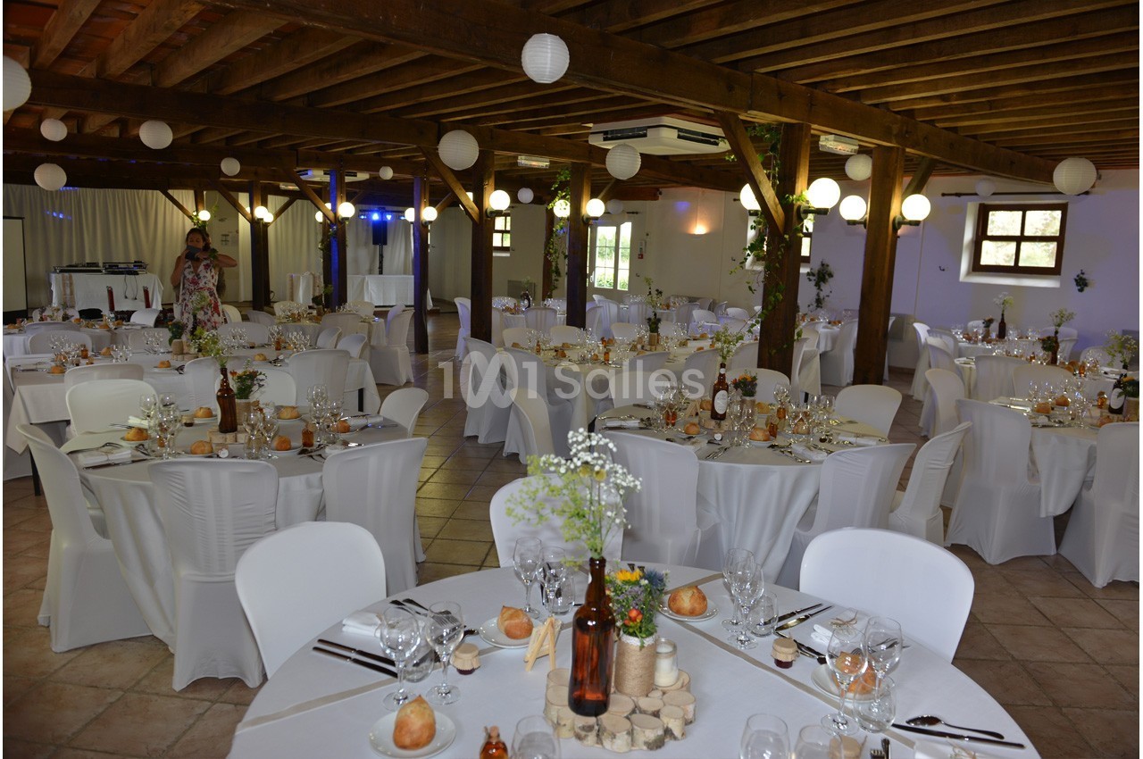 Salle de réception décorée avec des tables rondes dressées, nappes blanches et éclairage chaleureux.