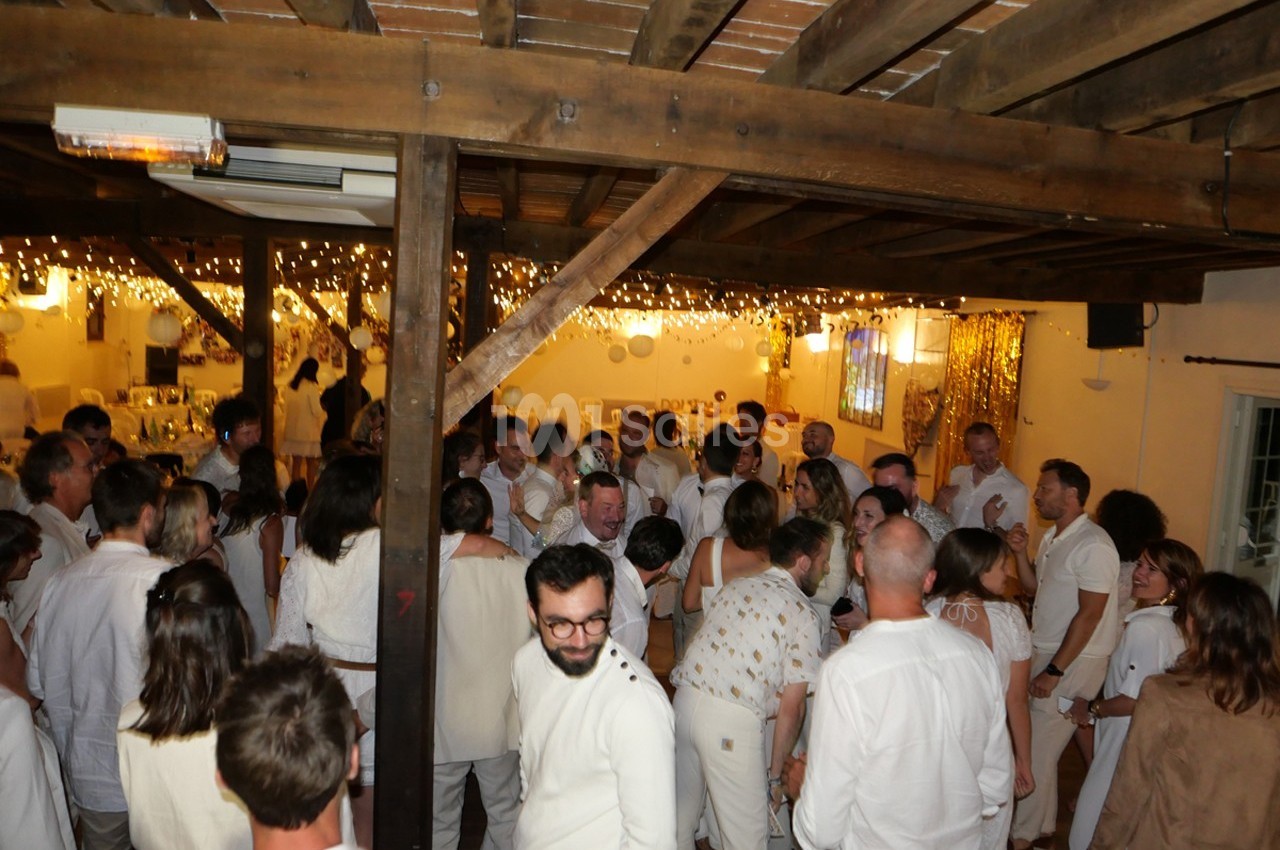 Groupe de personnes vêtues de blanc rassemblées dans une salle décorée de guirlandes lumineuses.