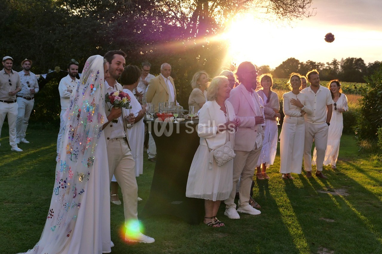 Un couple de mariés entouré d'invités en tenue claire lors d'une réception en plein air au coucher du soleil.