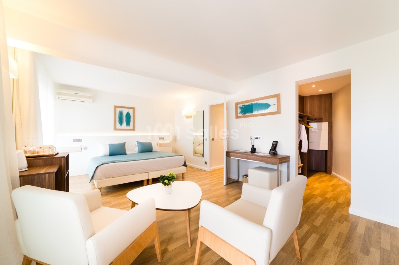 Chambre lumineuse avec lit double, coin salon, bureau, parquet clair et dressing ouvert.