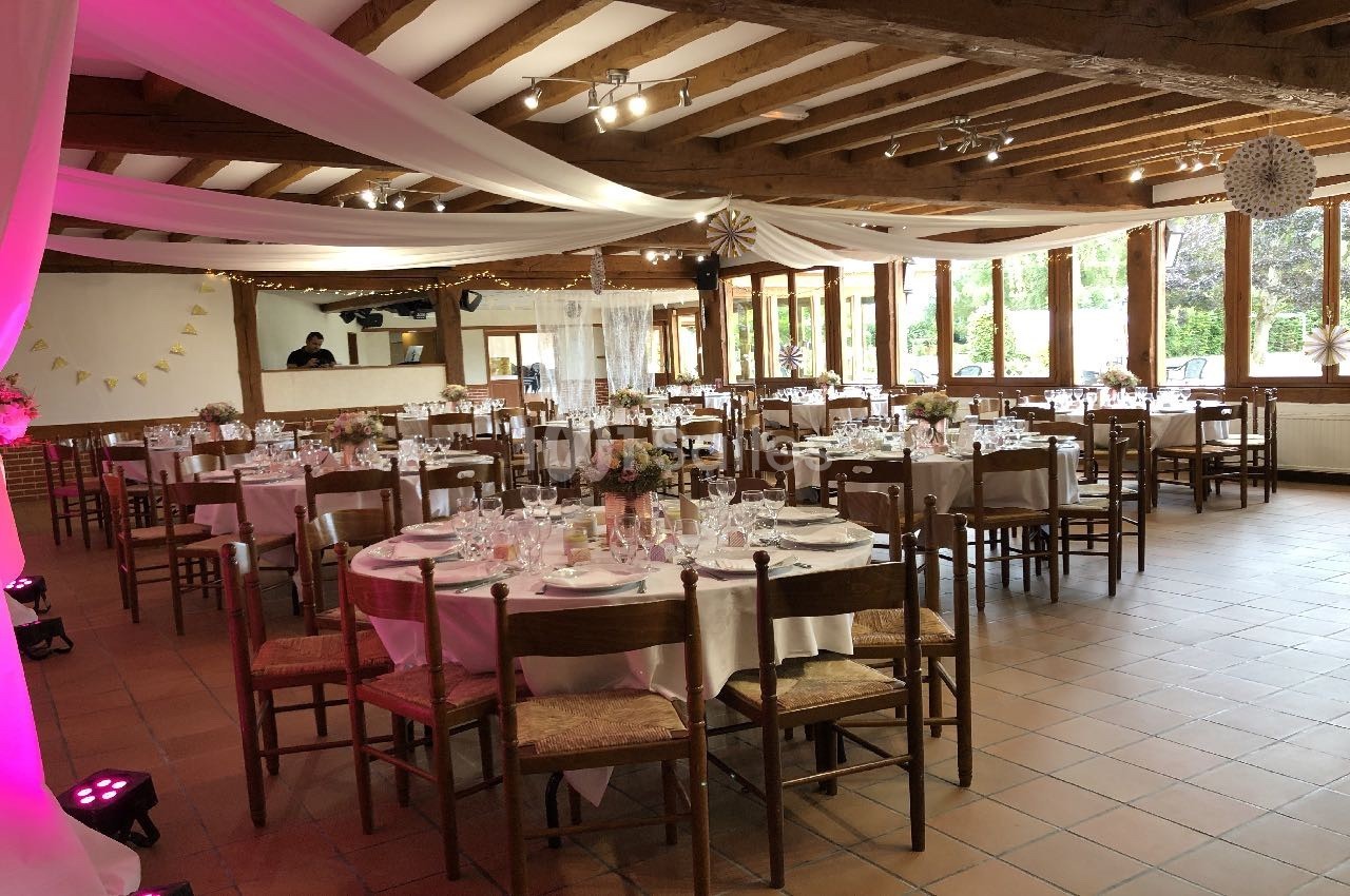 Salle de réception décorée avec des tables rondes dressées, des nappes blanches et des guirlandes suspendues.