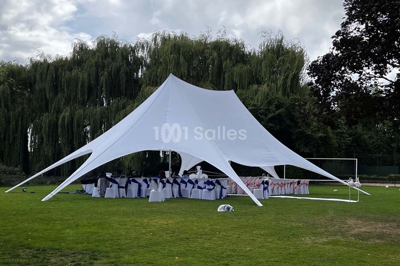 Grande tente blanche montée sur une pelouse, abritant des tables et des chaises décorées pour un événement en plein air.