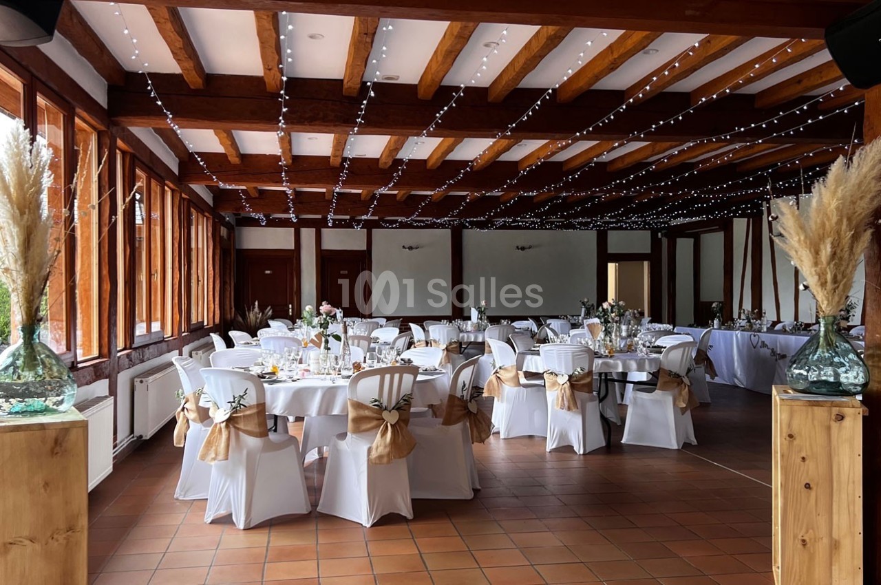 Salle de réception décorée avec des tables dressées, des chaises blanches ornées de nœuds et des guirlandes lumineuses au…