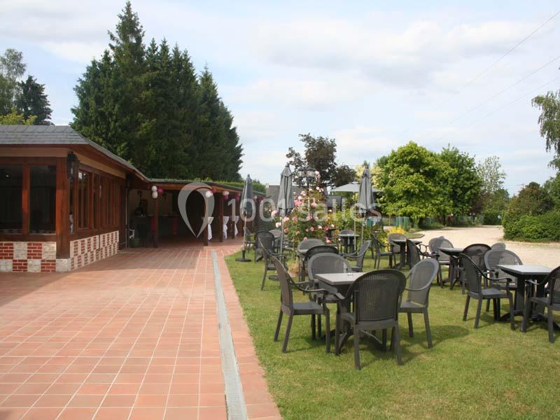 Terrasse extérieure avec tables et chaises en plastique, entourée de pelouse et d'arbres, par temps clair.