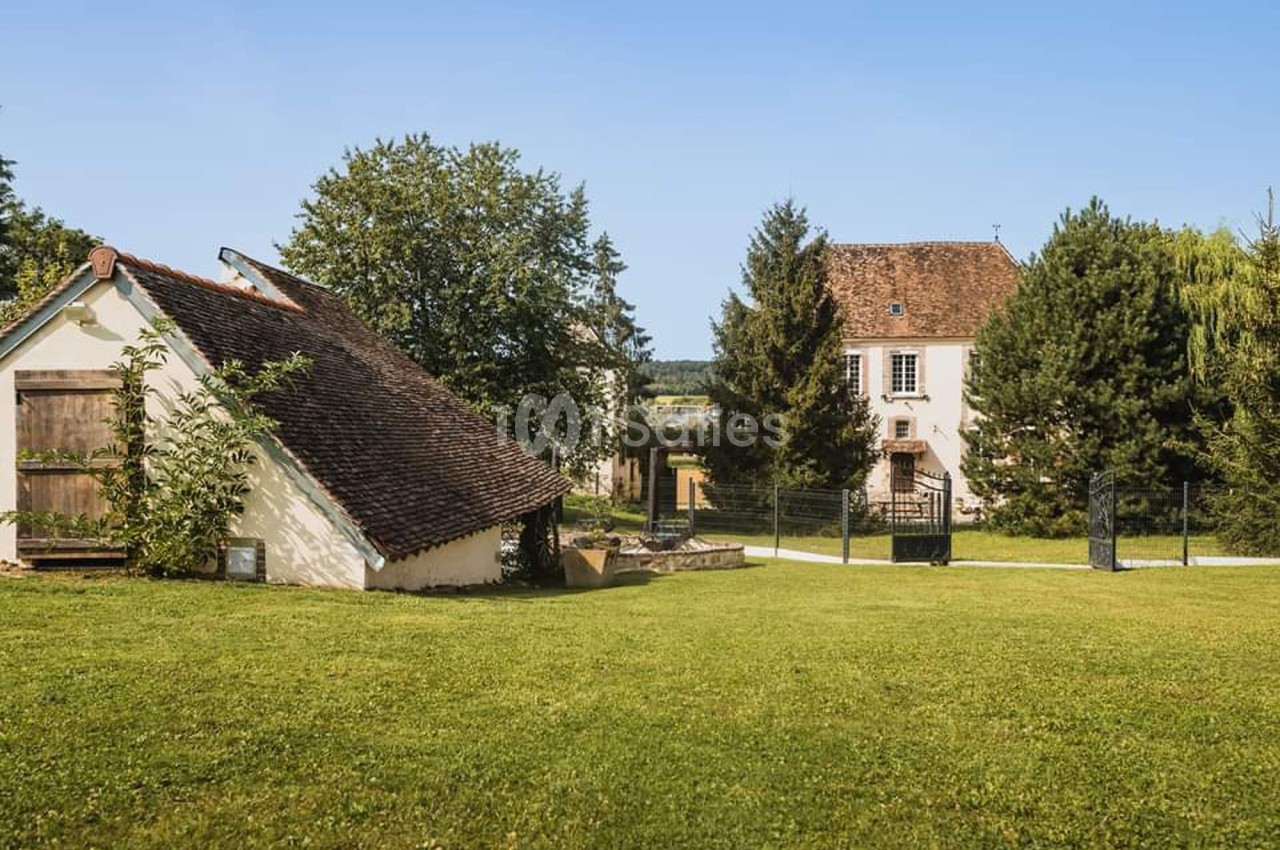 Deux maisons traditionnelles entourées de pelouses et d'arbres sous un ciel bleu clair.