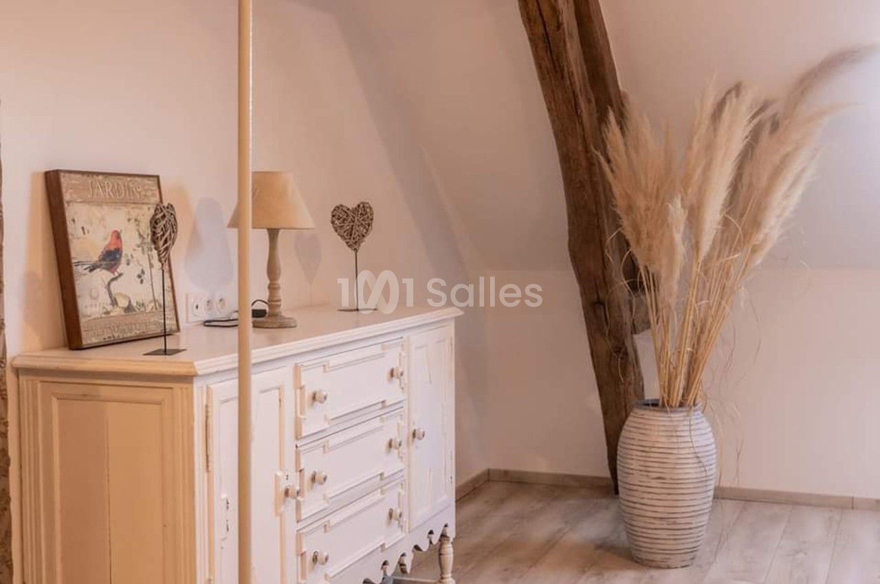 Commode blanche avec lampe et décorations, vase en céramique avec herbes séchées, poutre en bois visible.