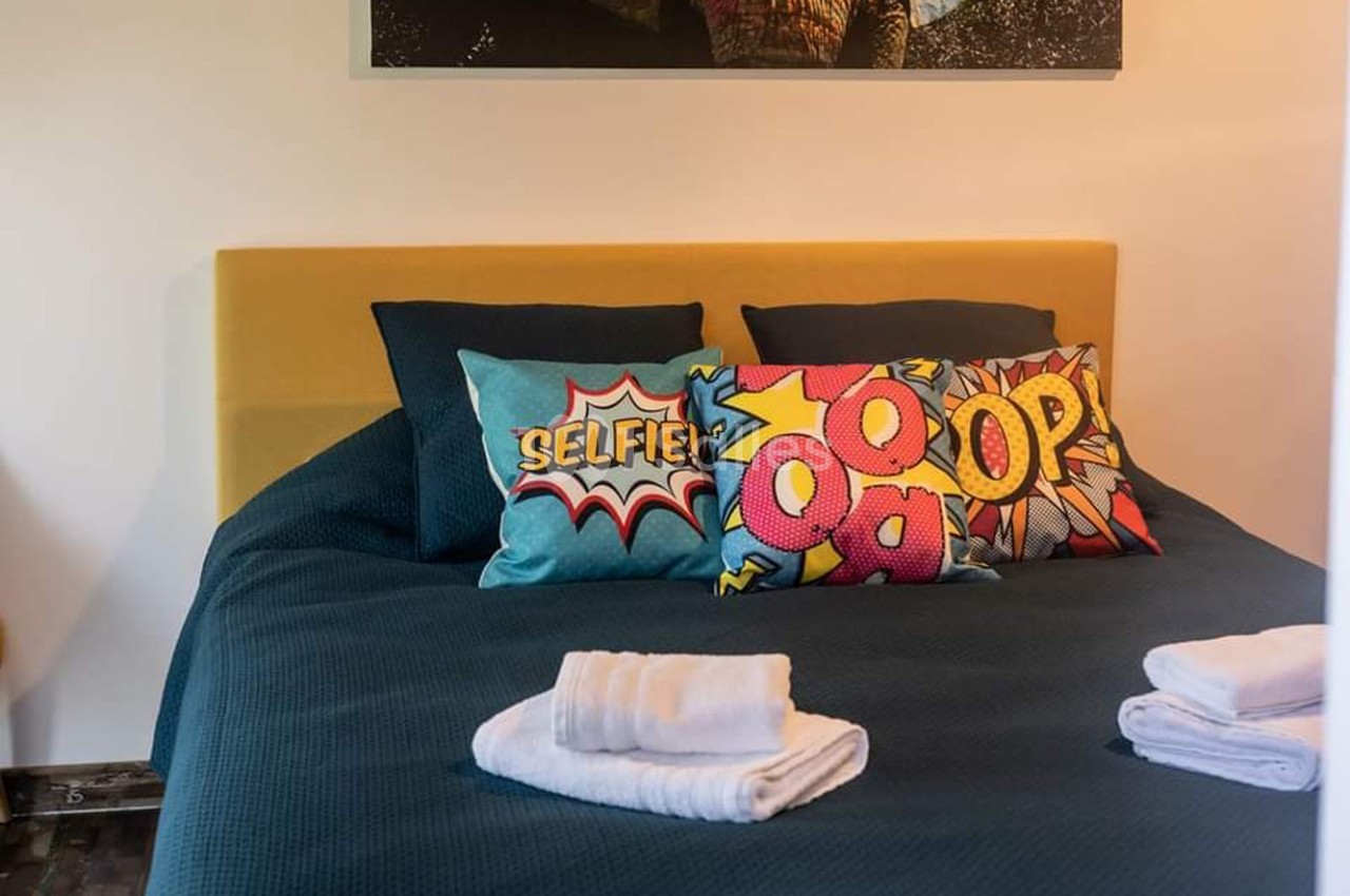 Lit avec tête de lit jaune, coussins colorés à motifs de bande dessinée et serviettes pliées au premier plan.