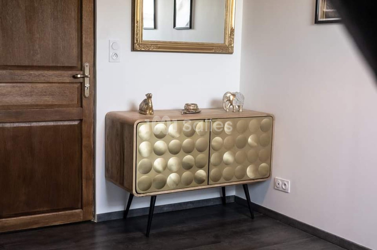 Buffet en bois avec portes dorées texturées, décoré de petites sculptures, placé près d'un miroir et d'une porte en bois.