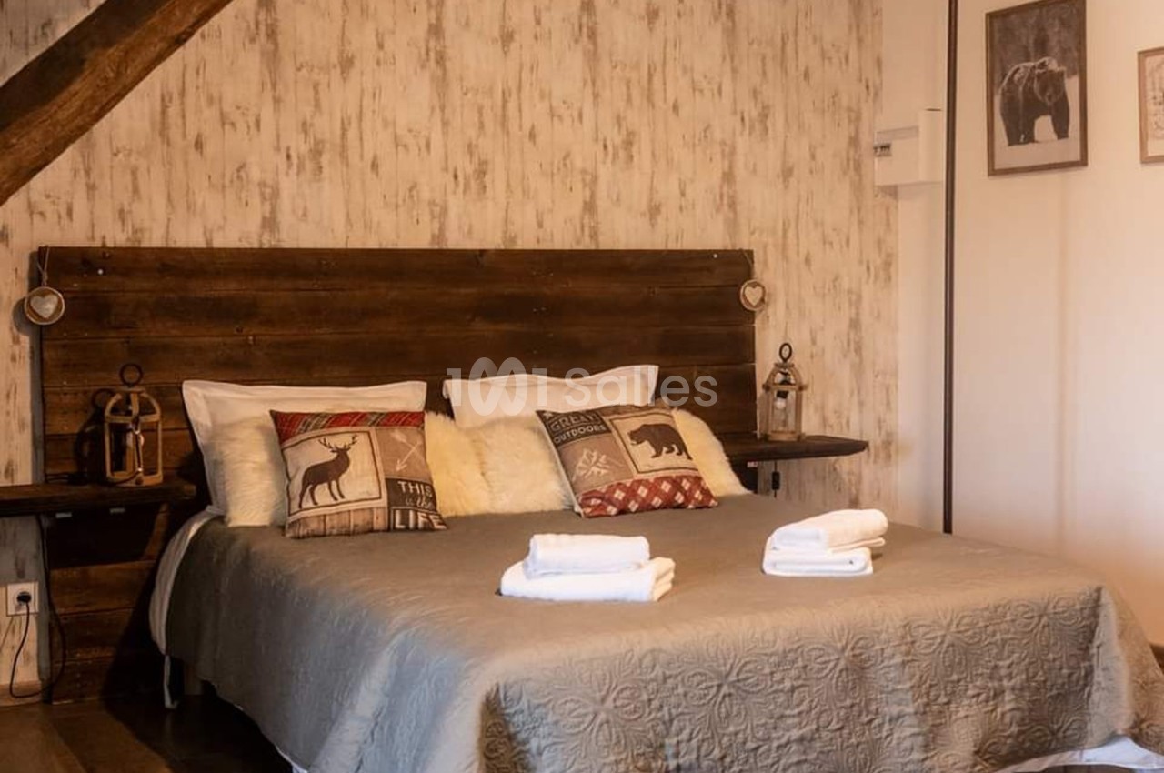 Lit double avec coussins décoratifs et serviettes pliées, dans une chambre rustique avec mur en bois et éclairage doux.